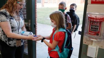 teacher and students practicing COVID-19 precautions before entering school